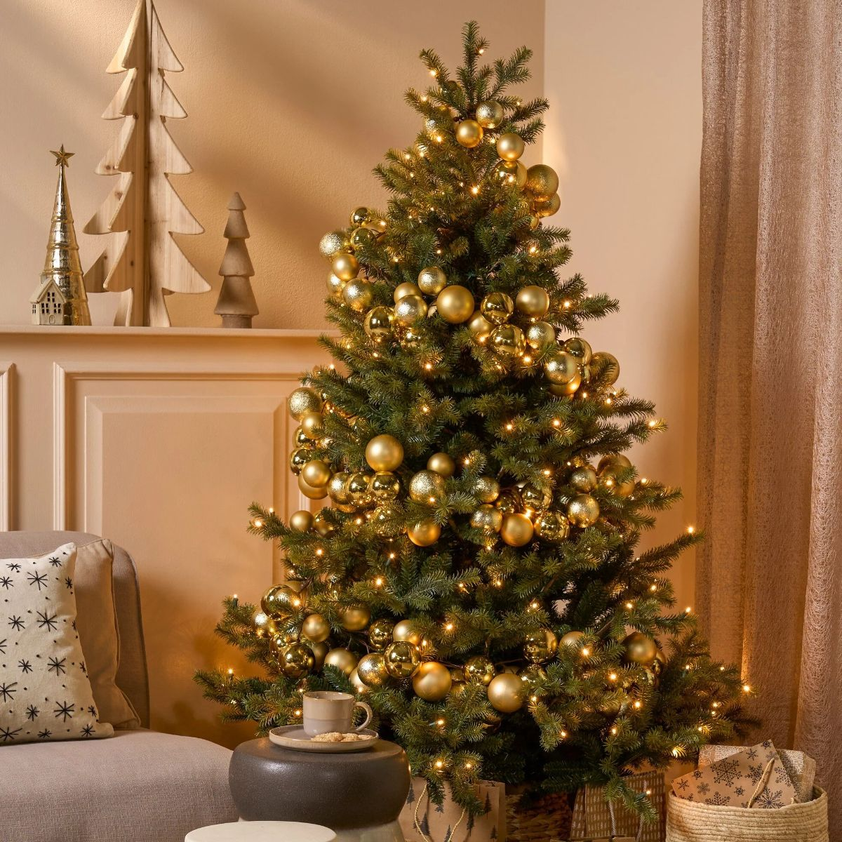 A Christmas tree decorated with gold ornaments, lights, and small wooden trees on a mantelpiece.