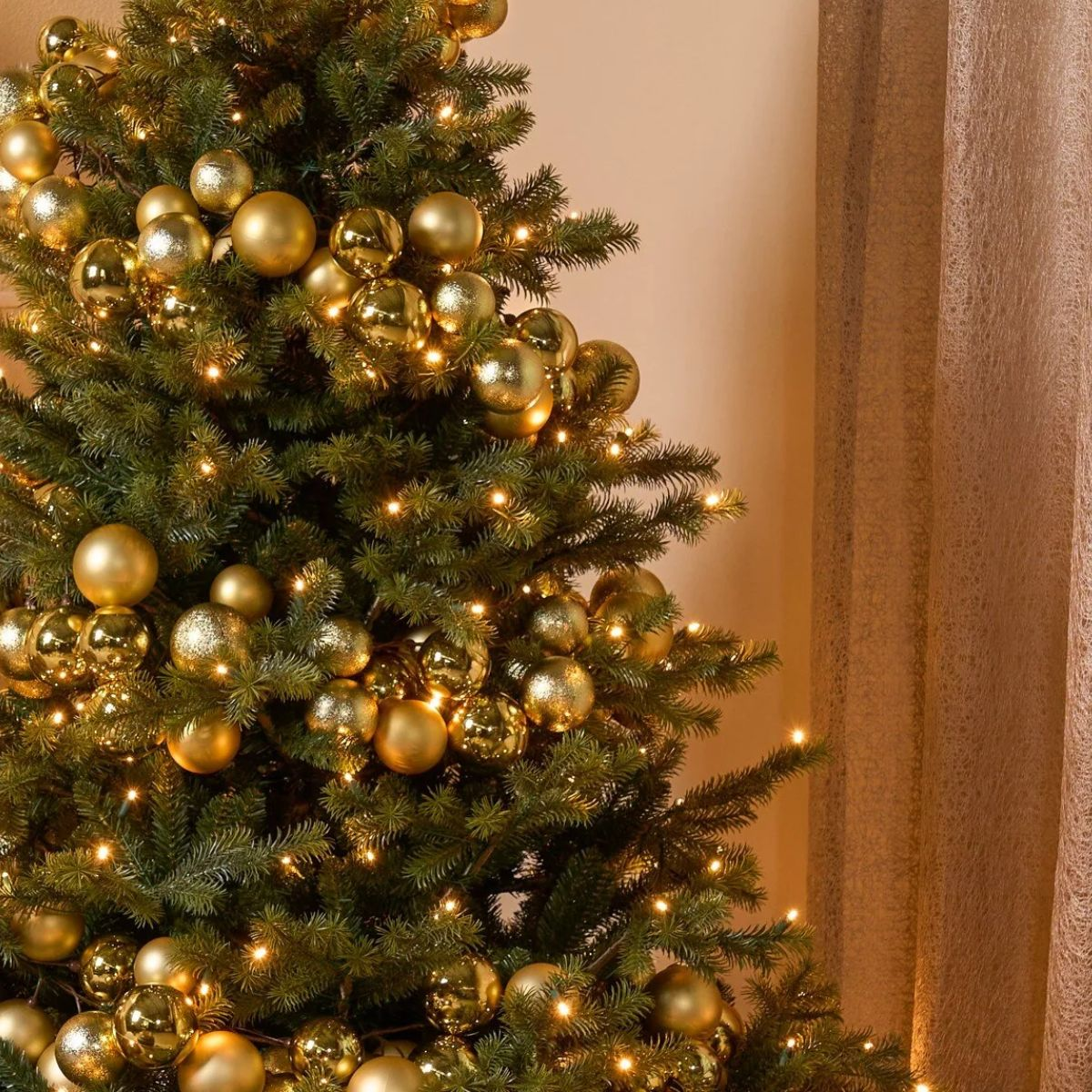 A green Christmas tree decorated with shiny gold ornaments and warm string lights.