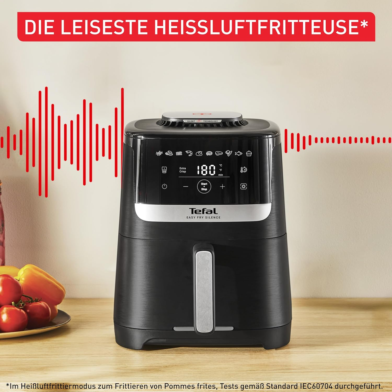 Schwarze Tefal Heißluftfritteuse auf einem Holztisch, umgeben von roten Wellenlinien und frischem Gemüse.