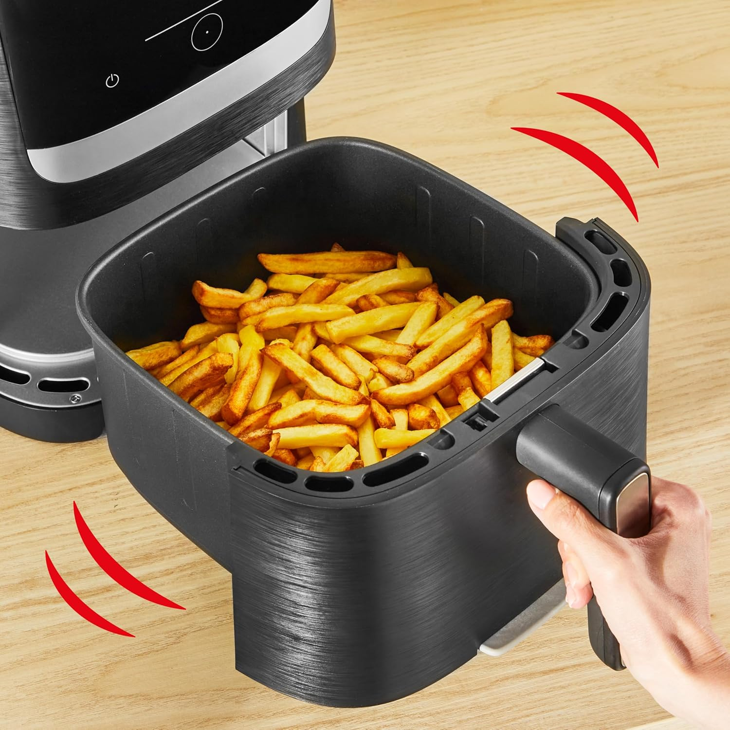 Eine Hand schüttelt den Korb einer Heißluftfritteuse, gefüllt mit goldbraunen Pommes frites.