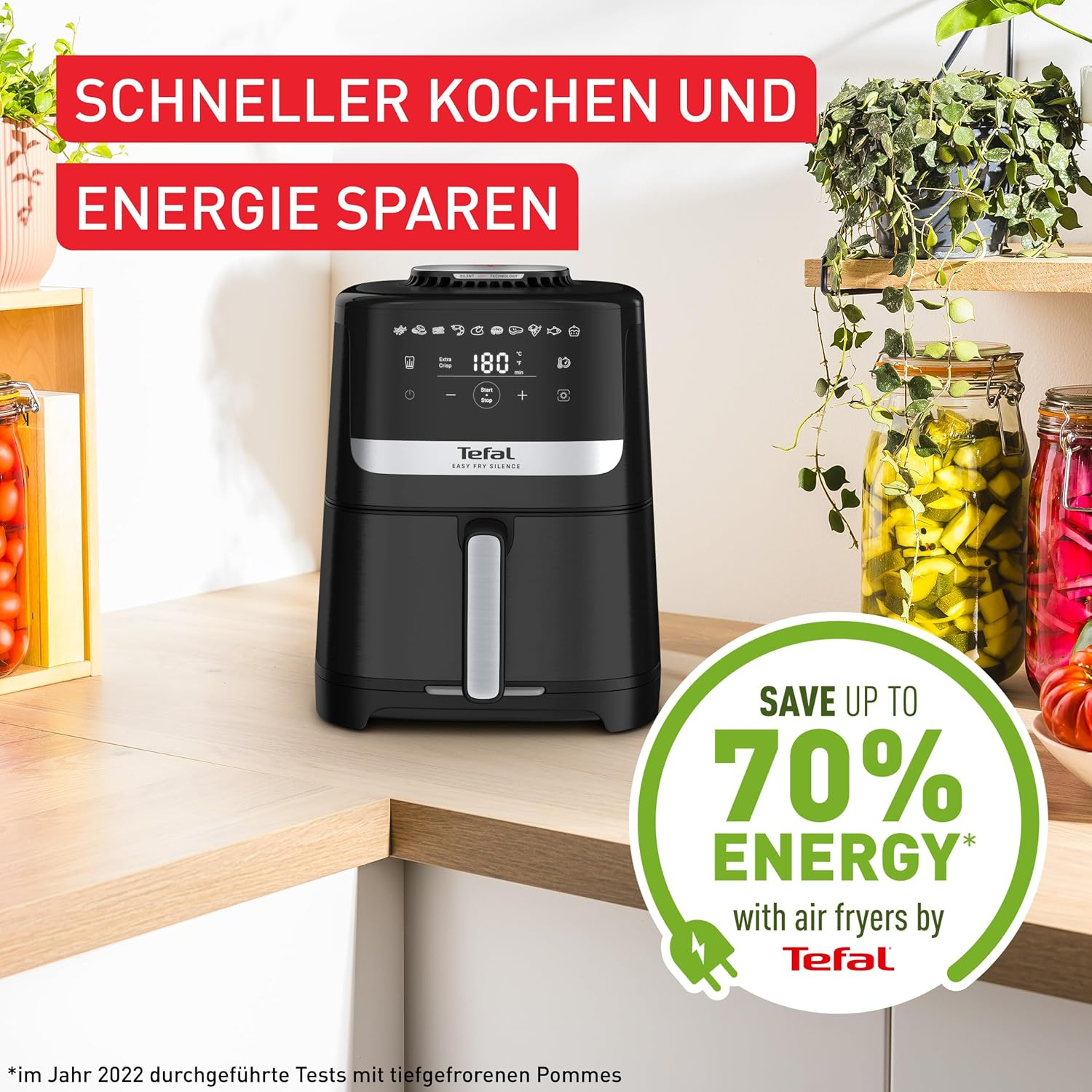 Eine schwarze Tefal Heißluftfritteuse steht auf einer Holztheke mit Text oben und Gläsern rechts.