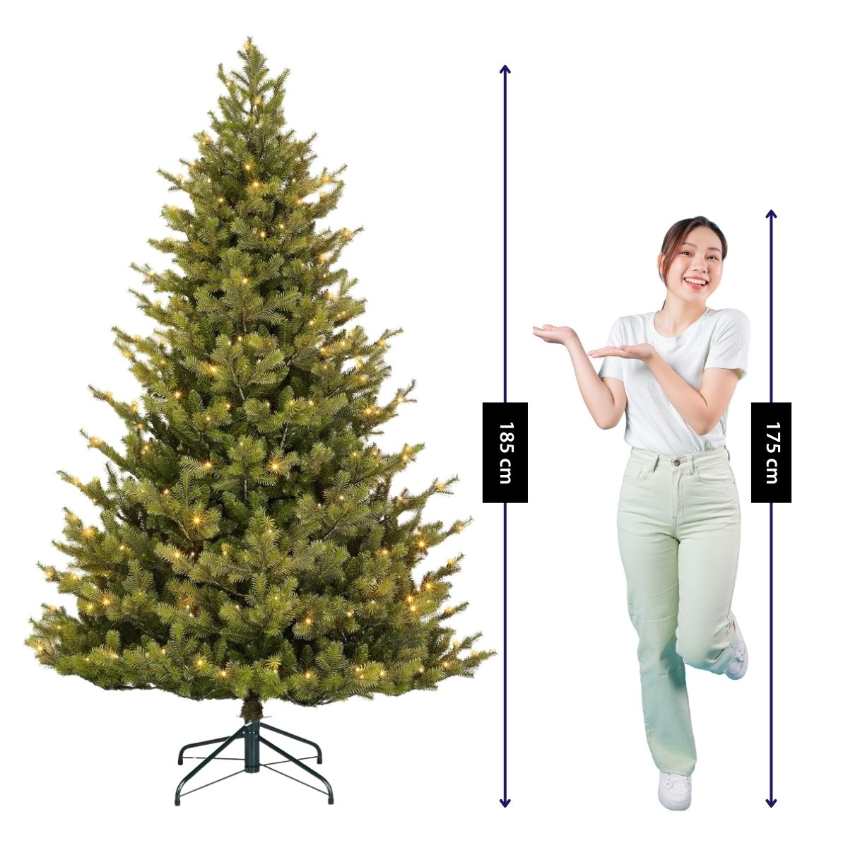 A woman in a white shirt and light pants stands next to a 185 cm tall artificial Christmas tree with lights.