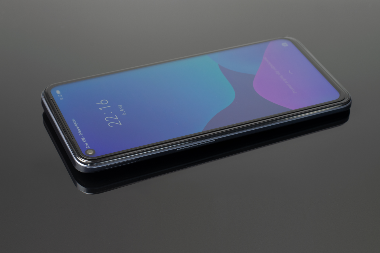 Smartfon z niebiesko-fioletowym wygaszaczem ekranu leży ukośnie na szarej, błyszczącej powierzchni.
