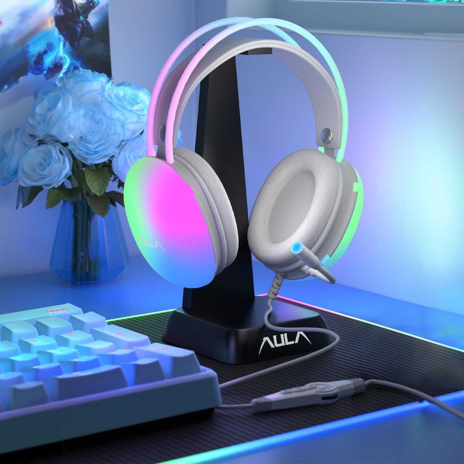 Cuffie da gioco bianche con illuminazione RGB su un supporto, accanto a rose blu e una tastiera.