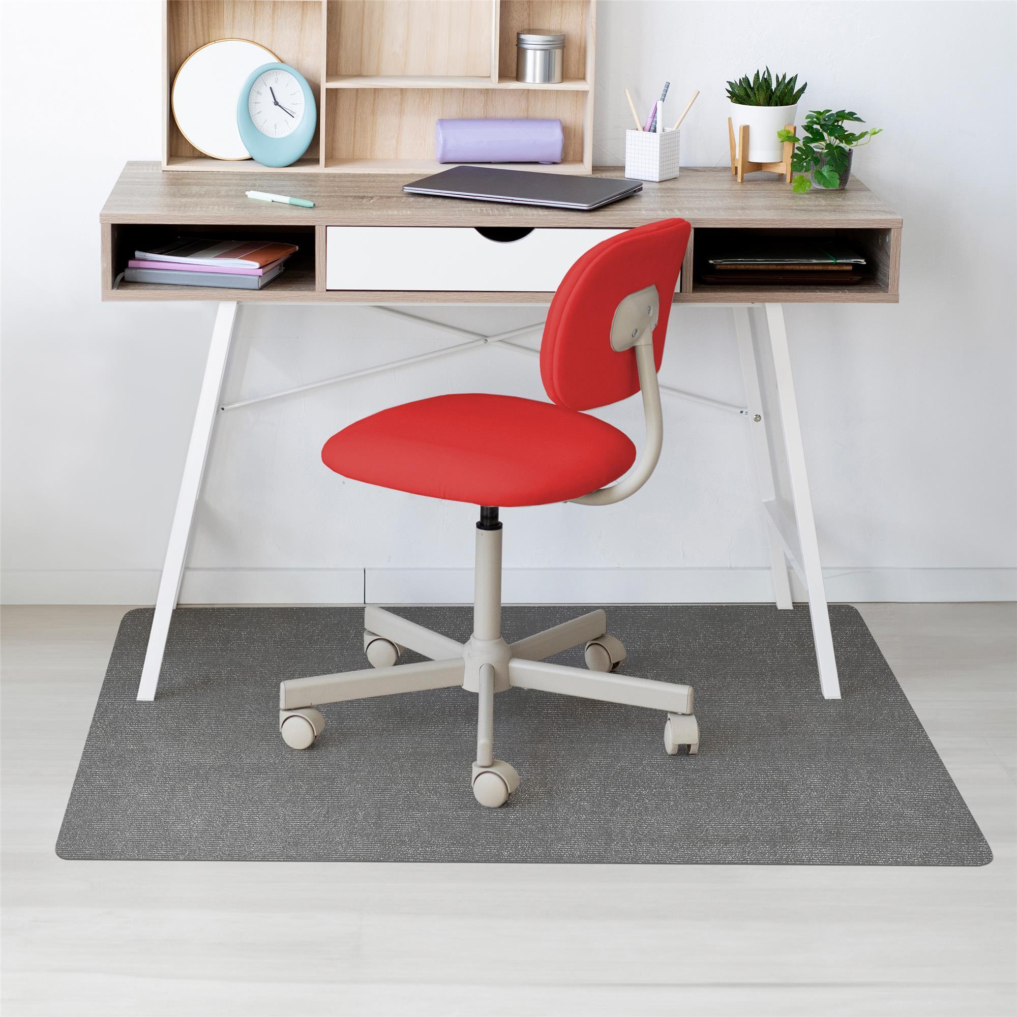 Ein roter Schreibtischstuhl steht vor einem holzfarbenen Schreibtisch mit Laptop, Regalen und Pflanzen auf einem grauen Teppich.