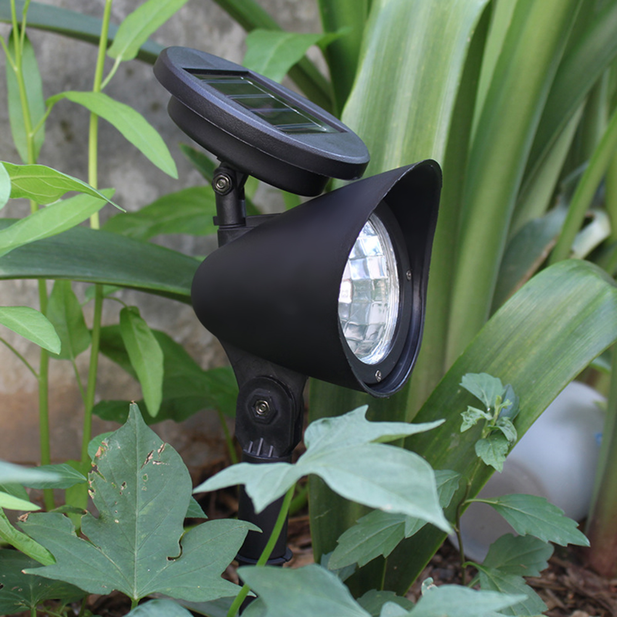 Eine schwarze Solarlampe steht im Garten umgeben von grünen Pflanzen.