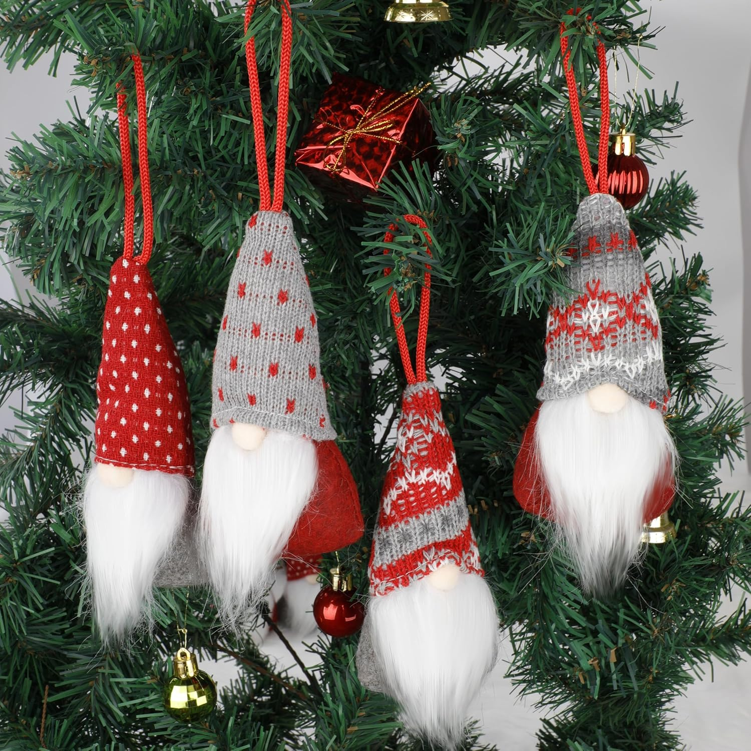 Vier kleine Weihnachtswichtel mit weißem Bart hängen an einer grünen Tanne.