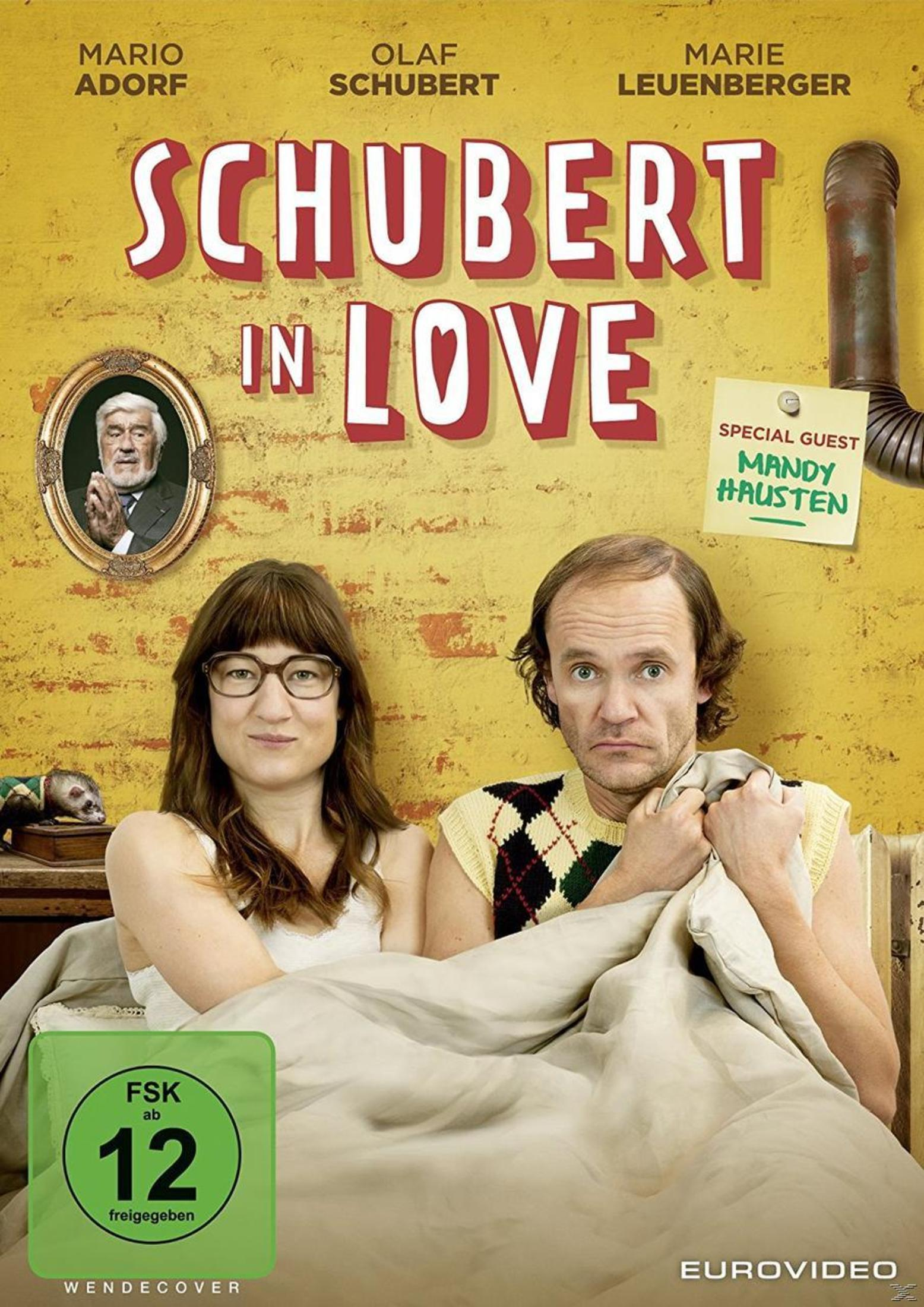 Filmplakat von 'Schubert in Love' mit Olaf Schubert und Marie Leuenberger in einem Bett vor gelber Ziegelwand.
