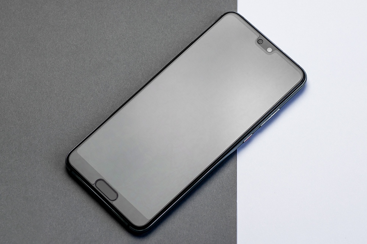 Smartfon spoczywa ukośnie na podzielonym tle w kolorze ciemnoszarym i białym.