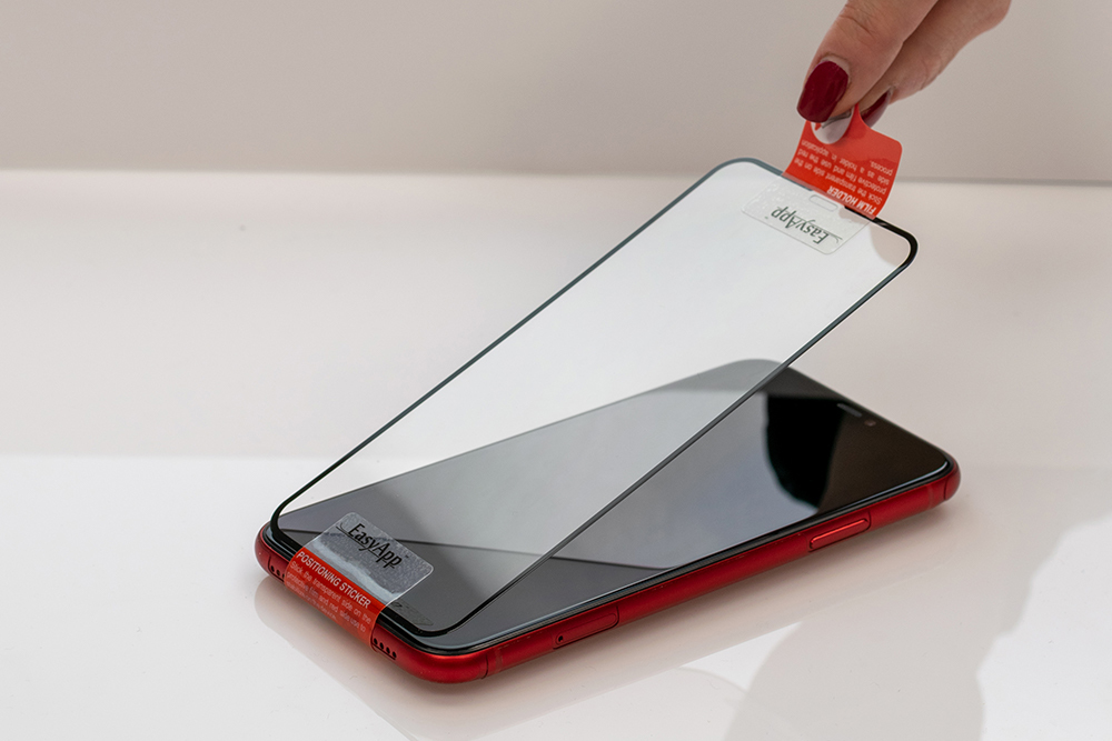 Ręka zdejmuje folię ochronną, aby nałożyć ją na czerwony smartfon.