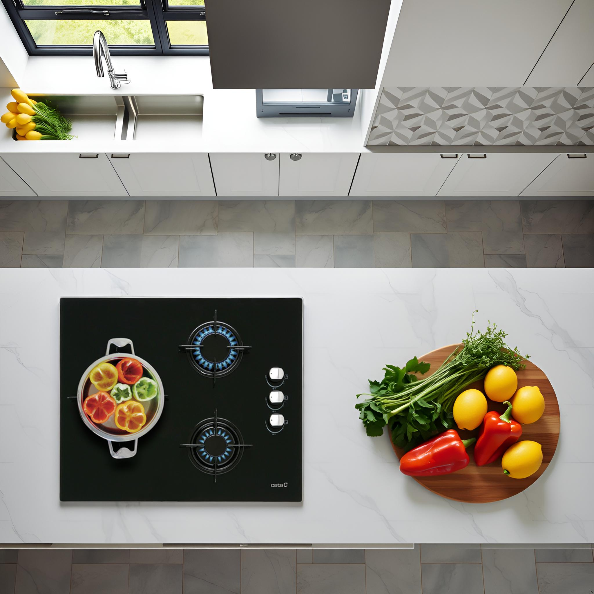 Vista cenital de una isla de cocina blanca con una placa de gas negra, una olla con verduras y una tabla de cortar.