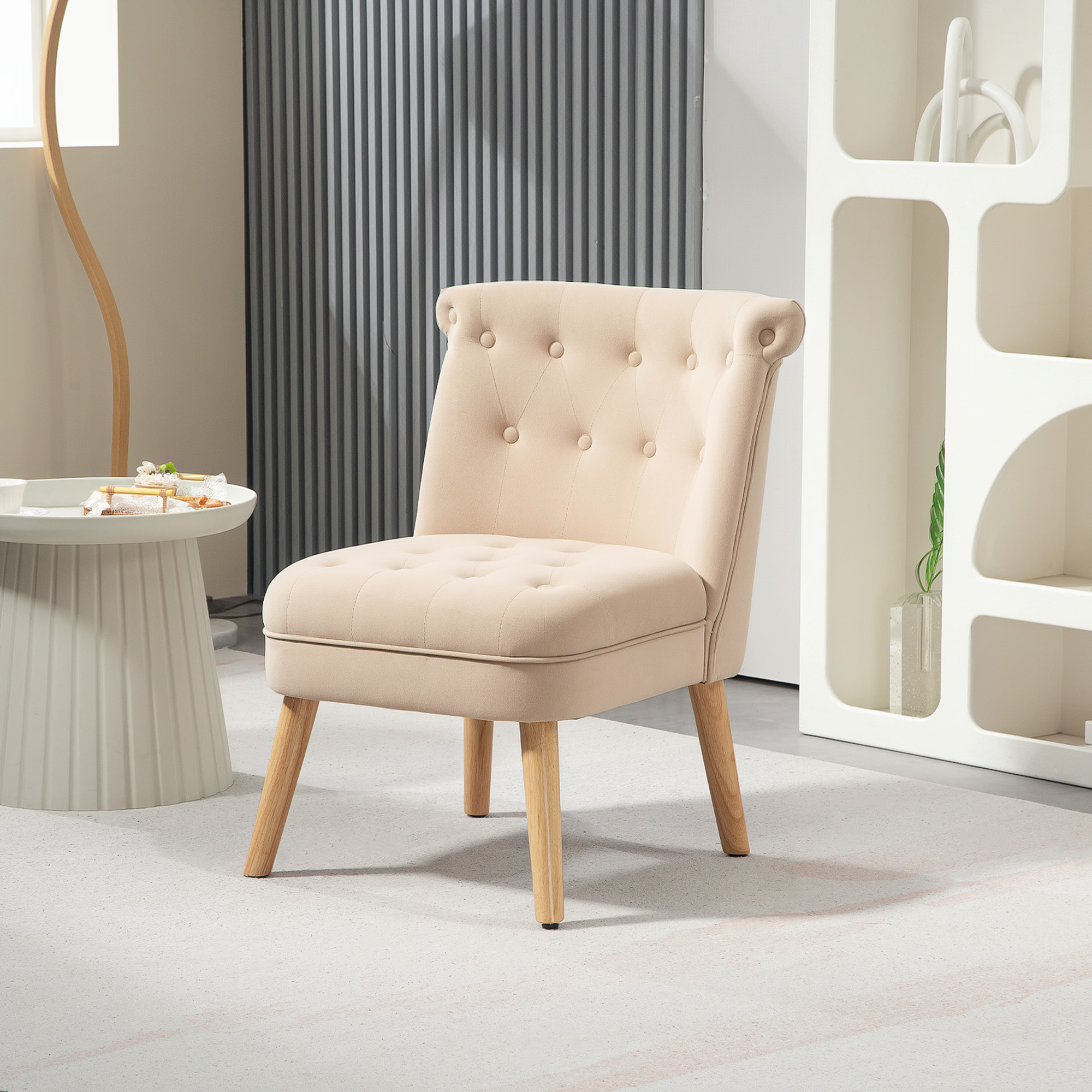Una poltrona beige capitonné con gambe in legno in una stanza luminosa con un tavolino e una libreria bianca moderna.