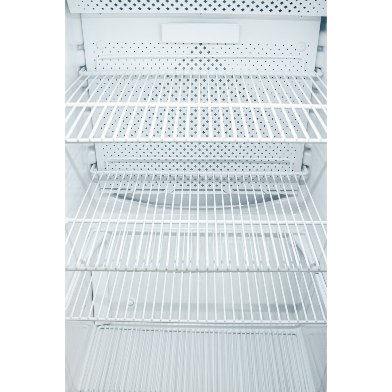 L'interno di un frigorifero vuoto con quattro ripiani in filo metallico bianco.
