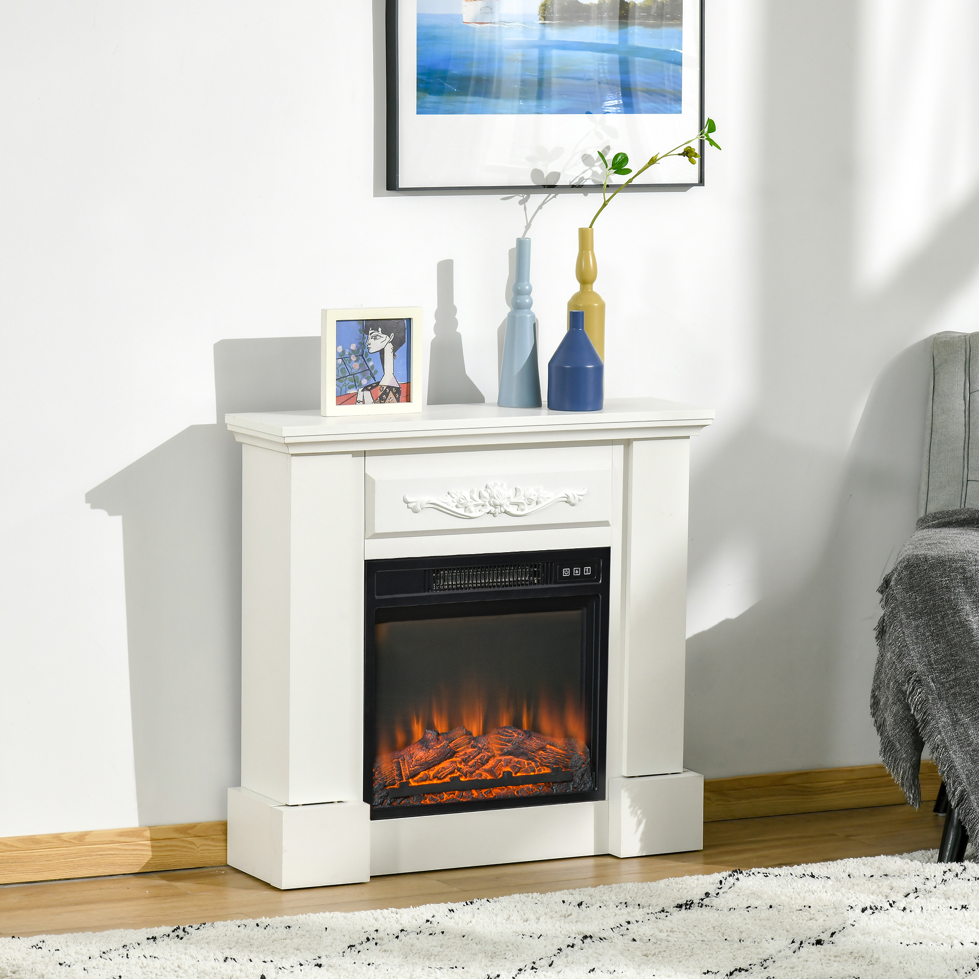 Chimenea eléctrica blanca con fuego falso, decorada con jarrones y cuadros en la pared.