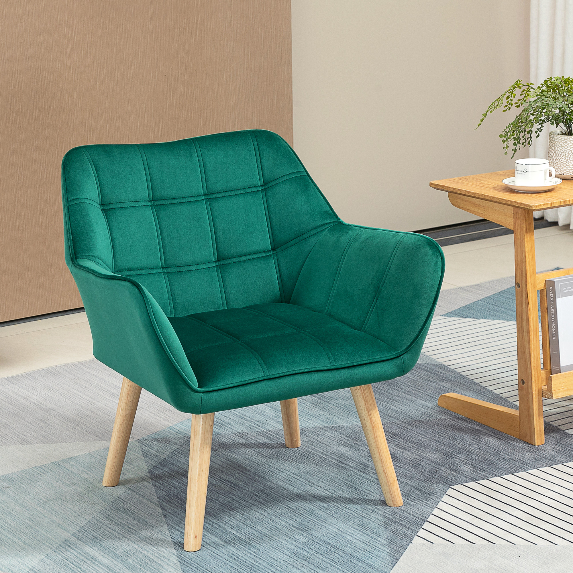 Una poltrona in velluto verde con gambe in legno si trova su un tappeto fantasia accanto a un piccolo tavolo.