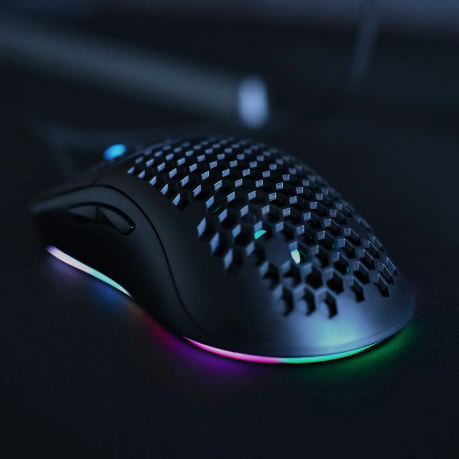 Un ratón de juego negro con patrón de panal e iluminación RGB colorida sobre una superficie oscura.