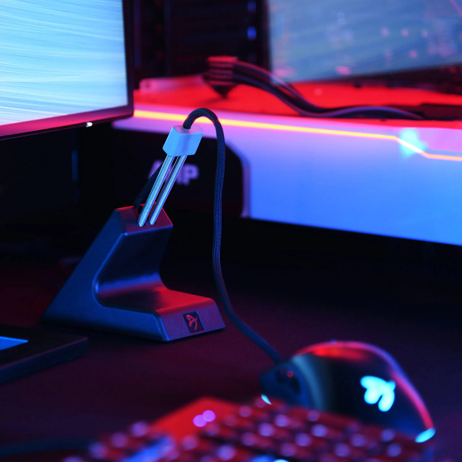 Ein schwarzer Maus-Bungee hält ein Kabel für eine Gaming-Maus vor blau-roter Kulisse.
