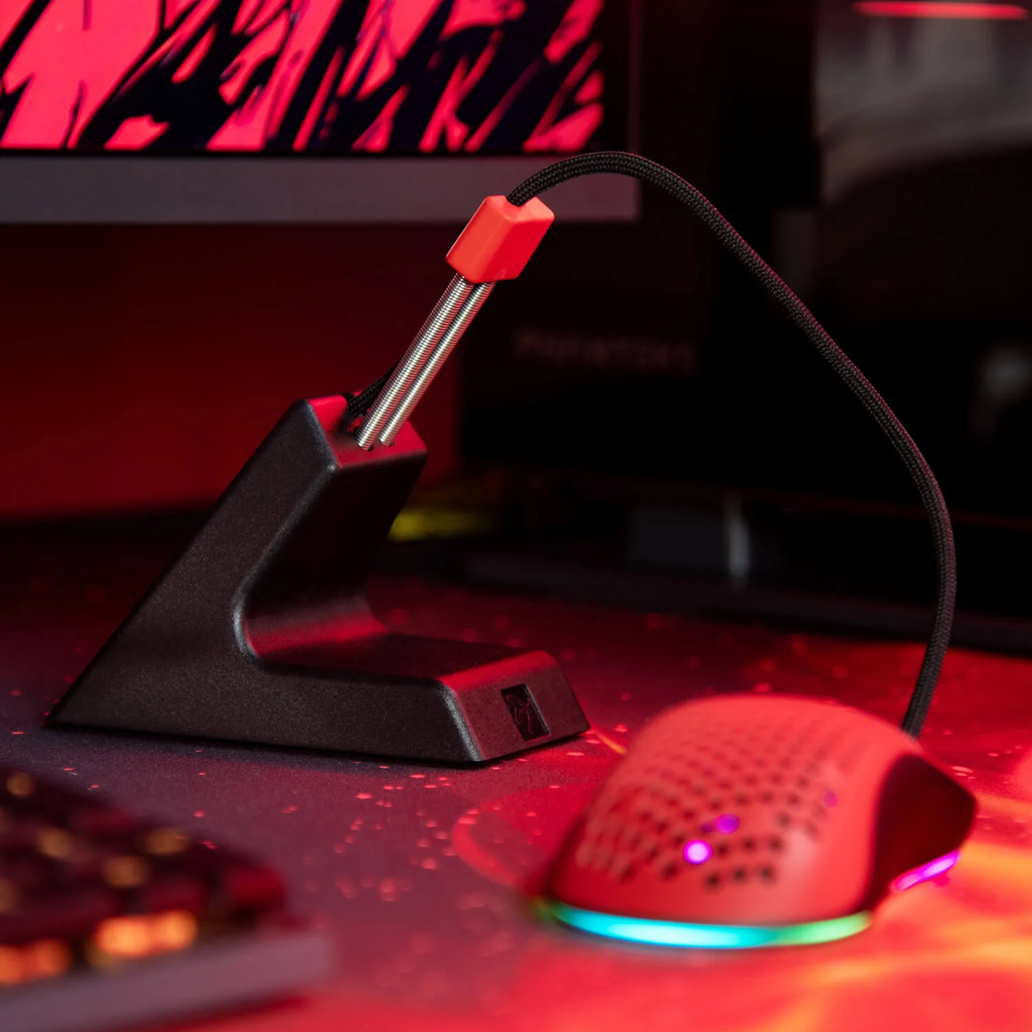 Ein schwarzer Maus-Bungee hält das Kabel einer roten Gaming-Maus auf einem beleuchteten Schreibtisch.