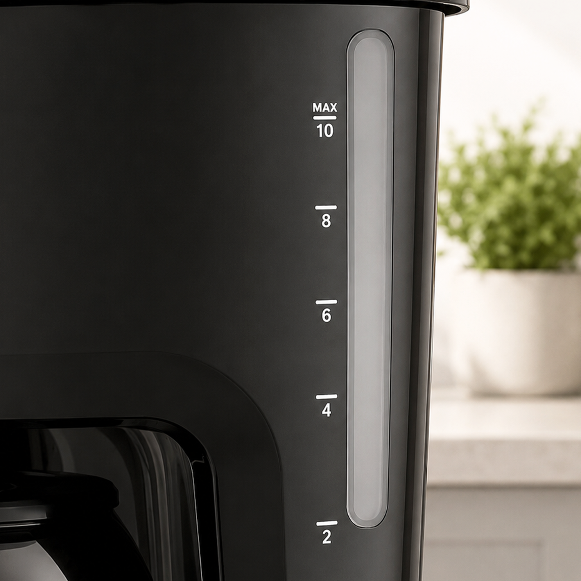 Black coffee maker with a water level indicator from 2 to MAX 10 cups, with a green potted plant in the background.