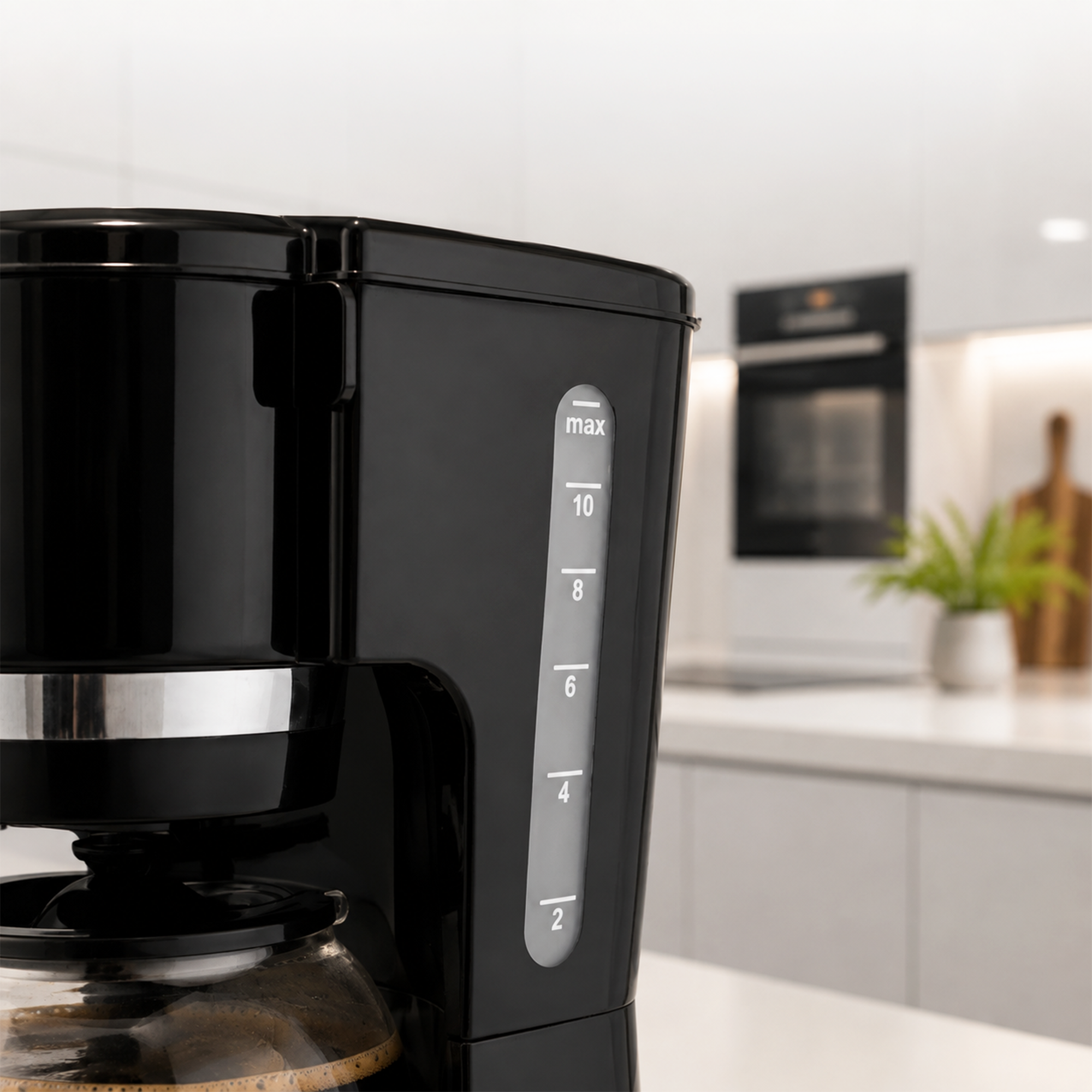 Black coffee maker on white counter with a water level indicator. Modern kitchen in the background.