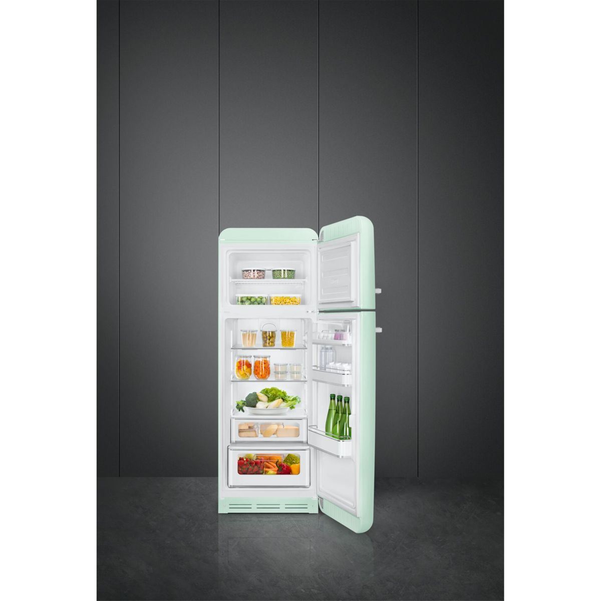 Un refrigerador abierto de color verde claro con comida en sus estantes se encuentra contra una pared oscura.
