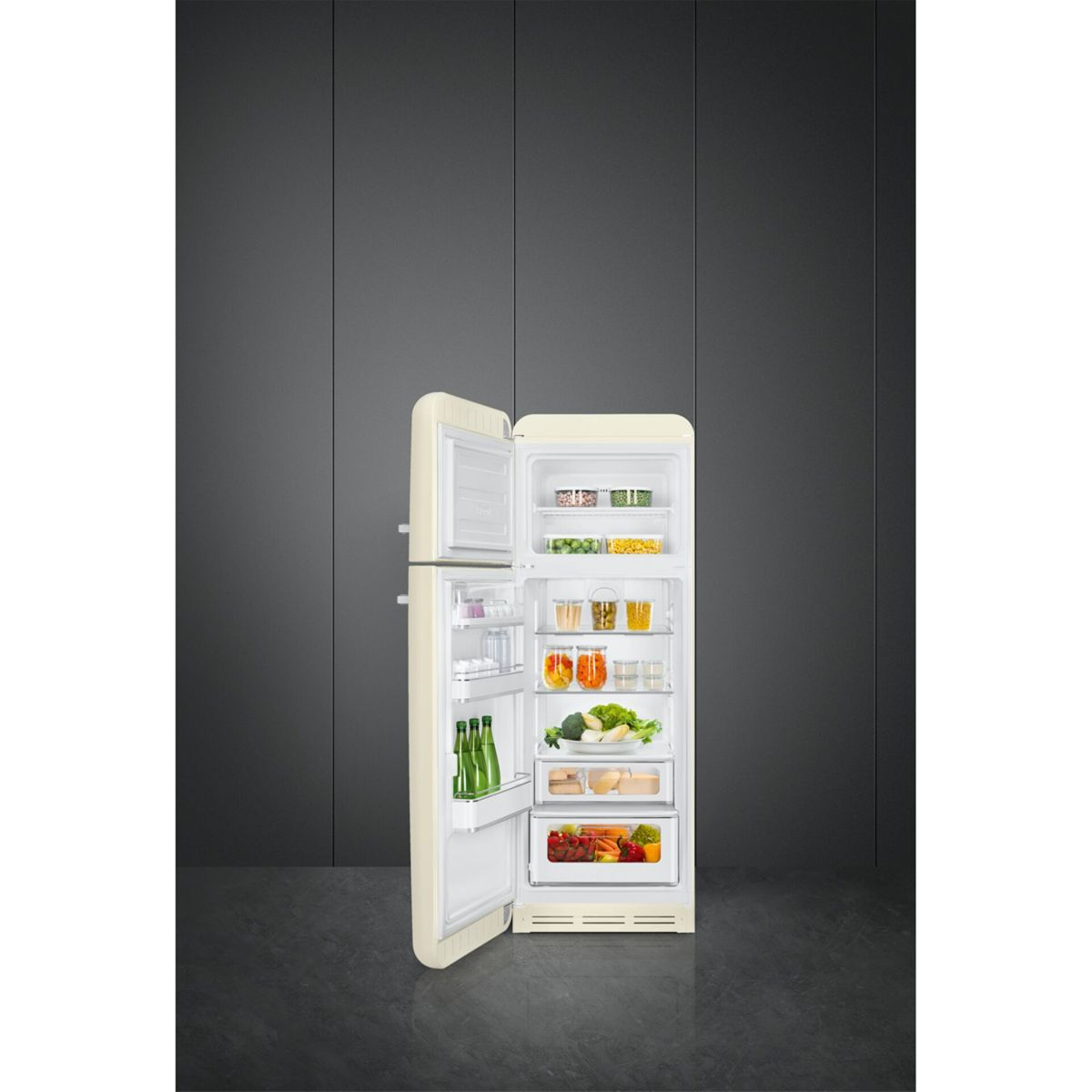 Un refrigerador retro color crema abierto con comida, en una habitación oscura con paredes grises.