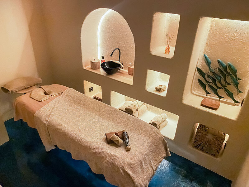 Una sala de spa con camillas de masaje, una pared con hornacinas iluminadas y un lavabo.