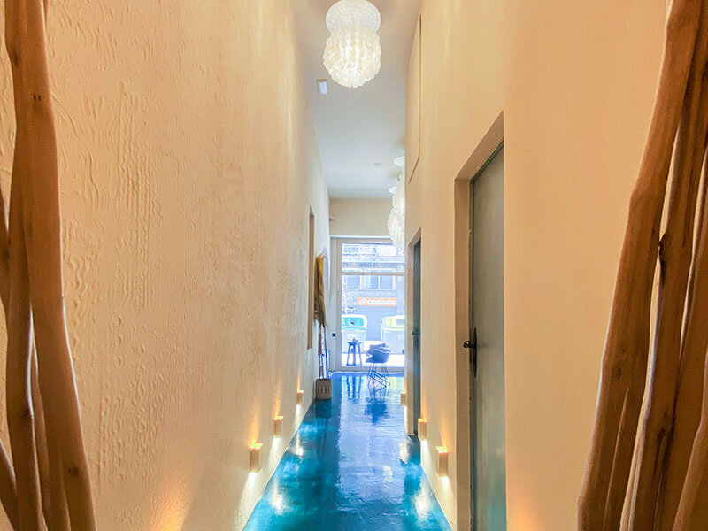 Largo pasillo con suelo azul brillante, paredes beiges, apliques de pared y puertas a la derecha.