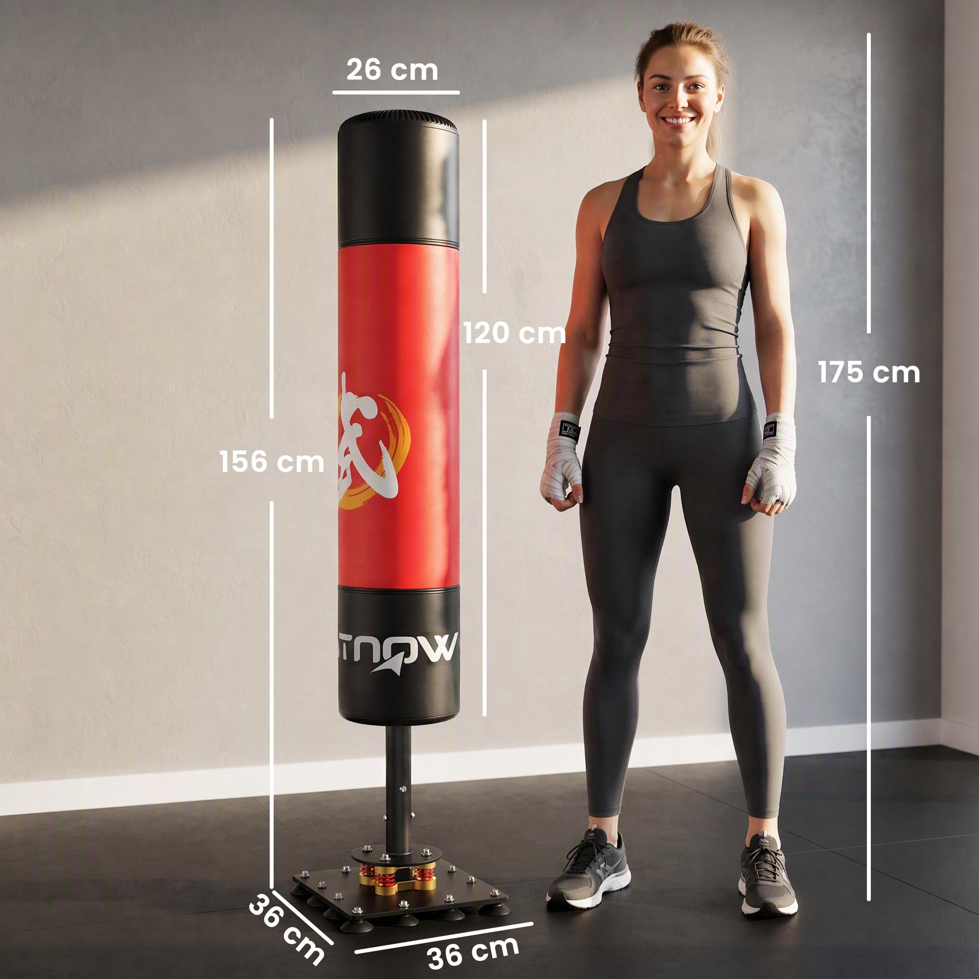 Una mujer en ropa deportiva junto a un saco de boxeo rojo y negro con medidas de altura.