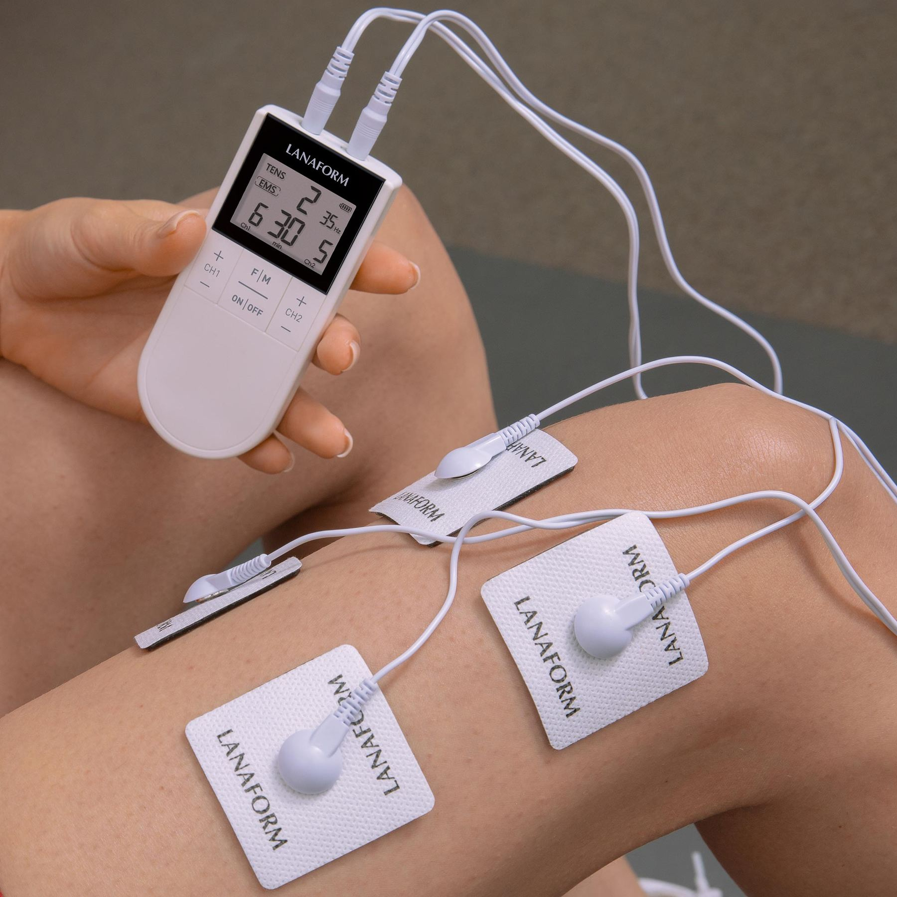 A person holds a white TENS device with electrode pads attached to their thigh and knee.