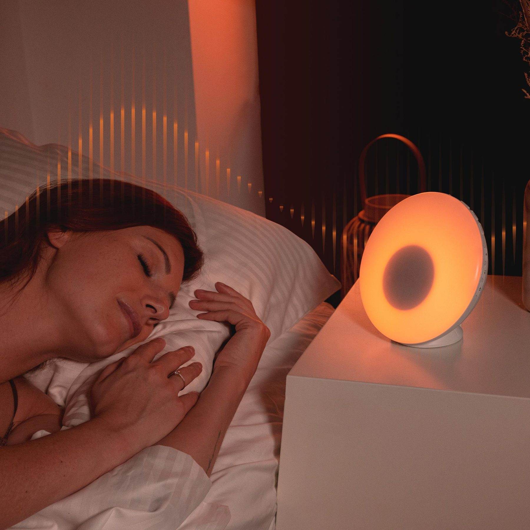 A woman peacefully sleeps in bed while a glowing round orange light sits on the nightstand beside her.
