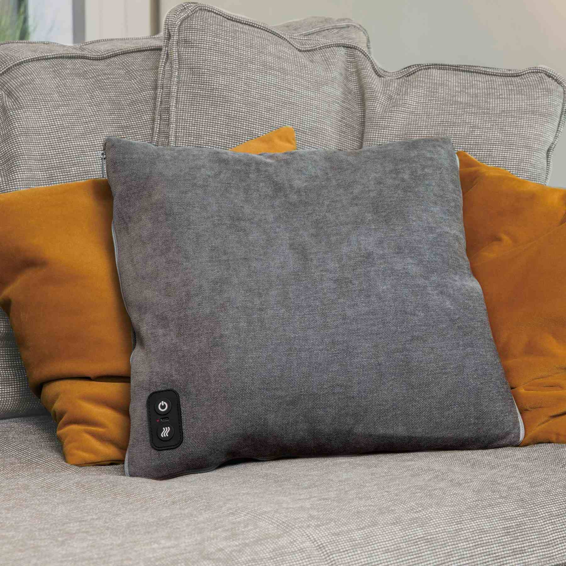 Ein graues Kissen mit Steuerelement auf einem Sofa vor senfgelben Kissen.