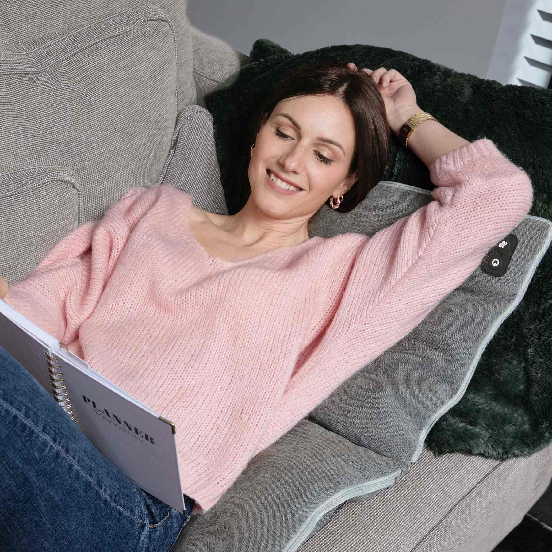 Frau in rosa Pullover liegt gemütlich auf einem Sofa und liest in einem Planer.