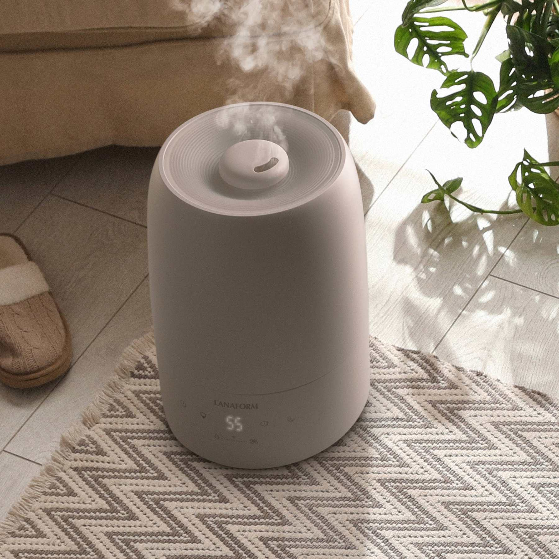 A white humidifier emitting vapor on a patterned rug in a room with a potted plant and slipper.