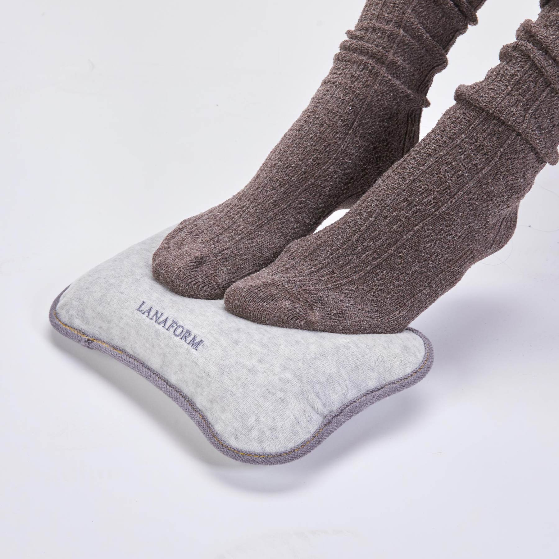 Füße in braunen Socken stehen auf einem grauen Lanaform Kissen.