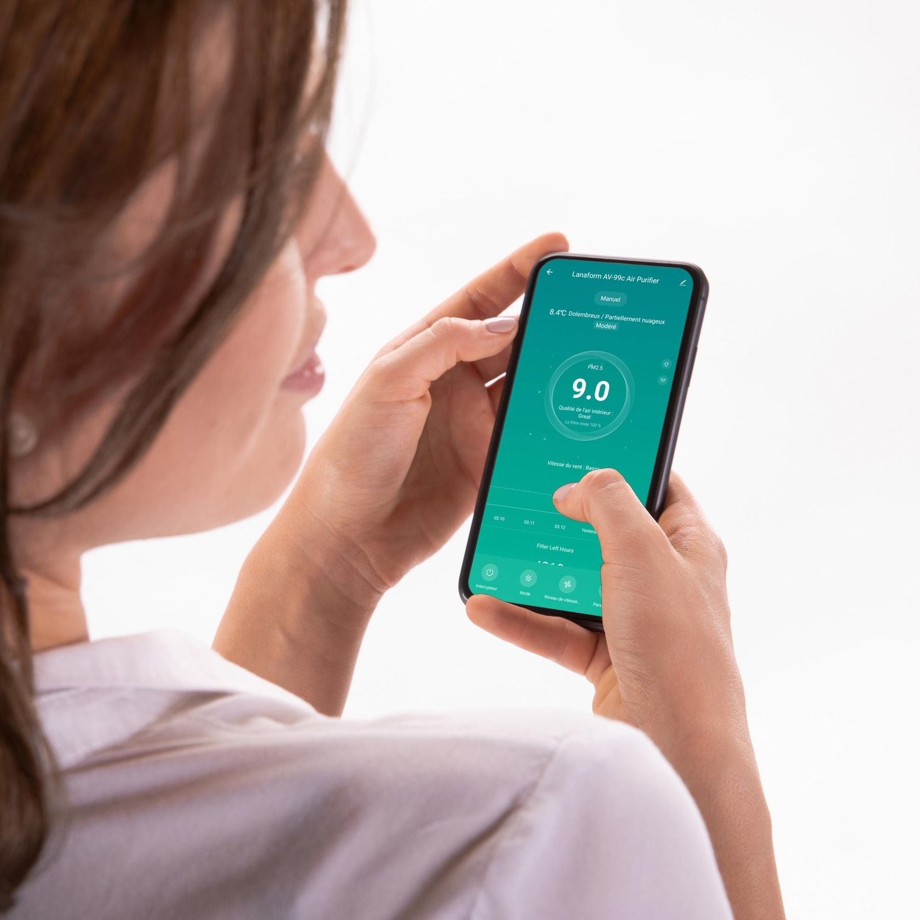 A woman holding a smartphone displaying a green air purifier control app.