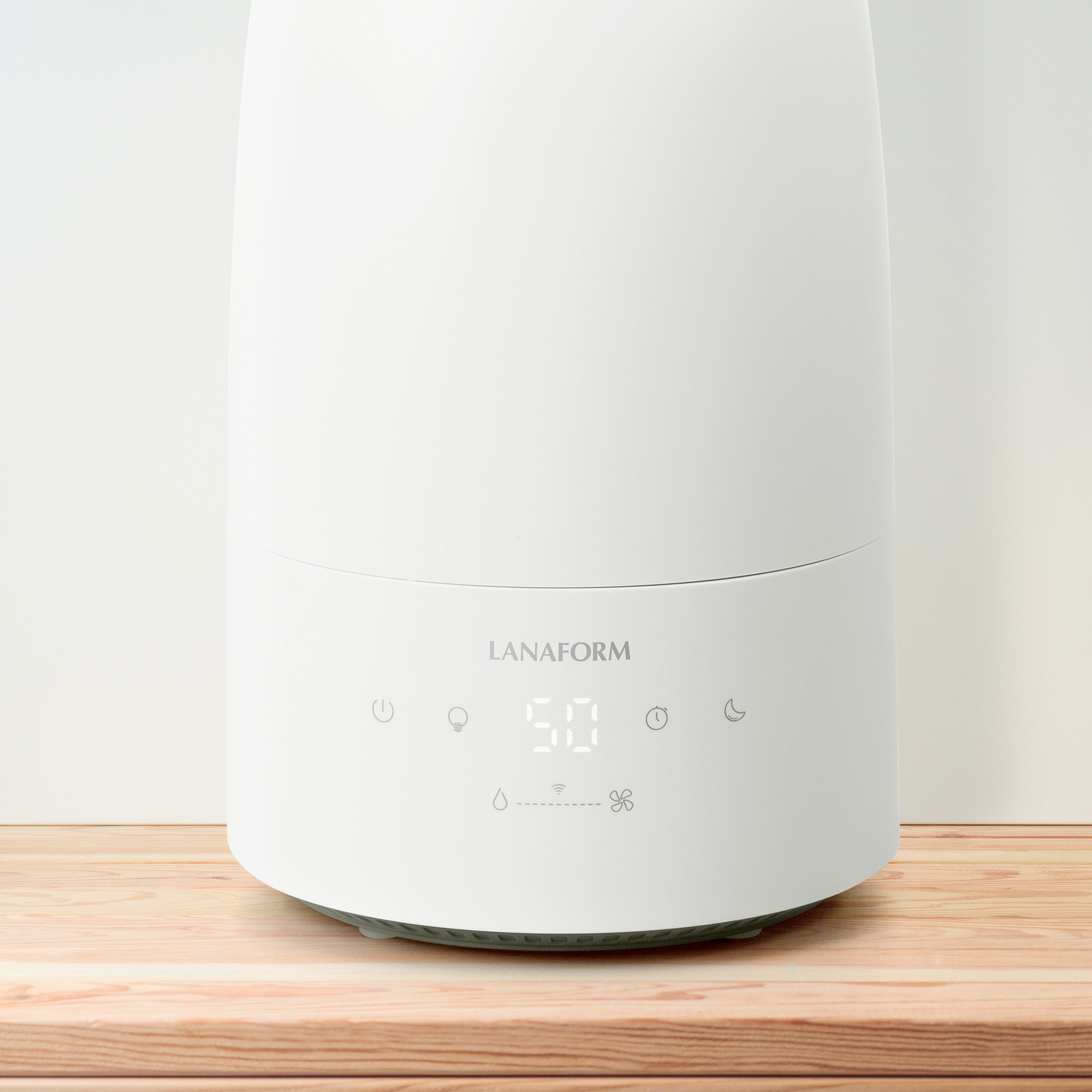 A white Lanaform humidifier with a digital display and touch icons stands on a wooden surface against a white wall.