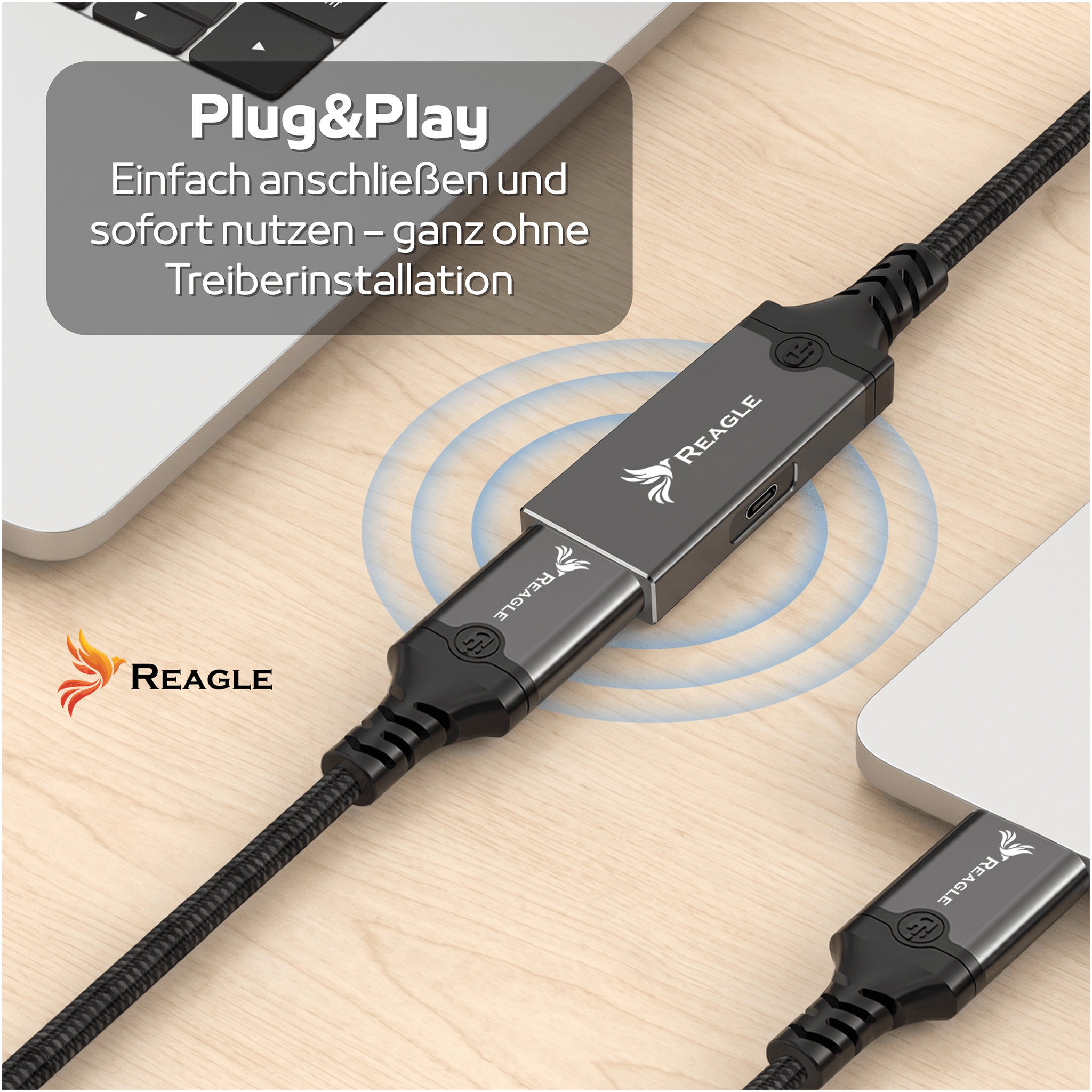 Un cable USB Reagle descansa sobre un escritorio de madera junto a portátiles, con texto.