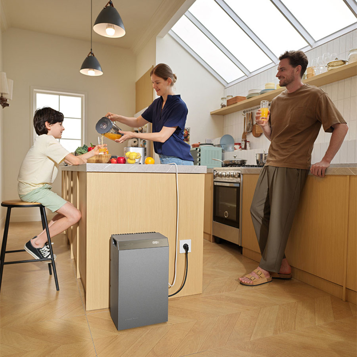 Eine Familie in einer hellen Küche, ein Kind sitzt auf einem Hocker, während eine Frau Saft in ein Glas gießt.