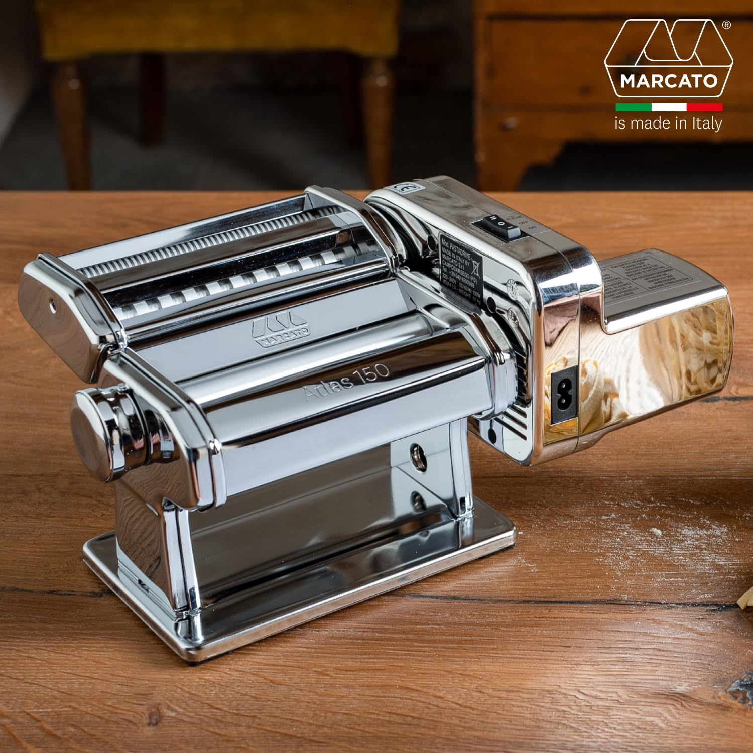 Une machine à pâtes Marcato Atlas 150 chromée avec moteur est posée sur une table en bois.