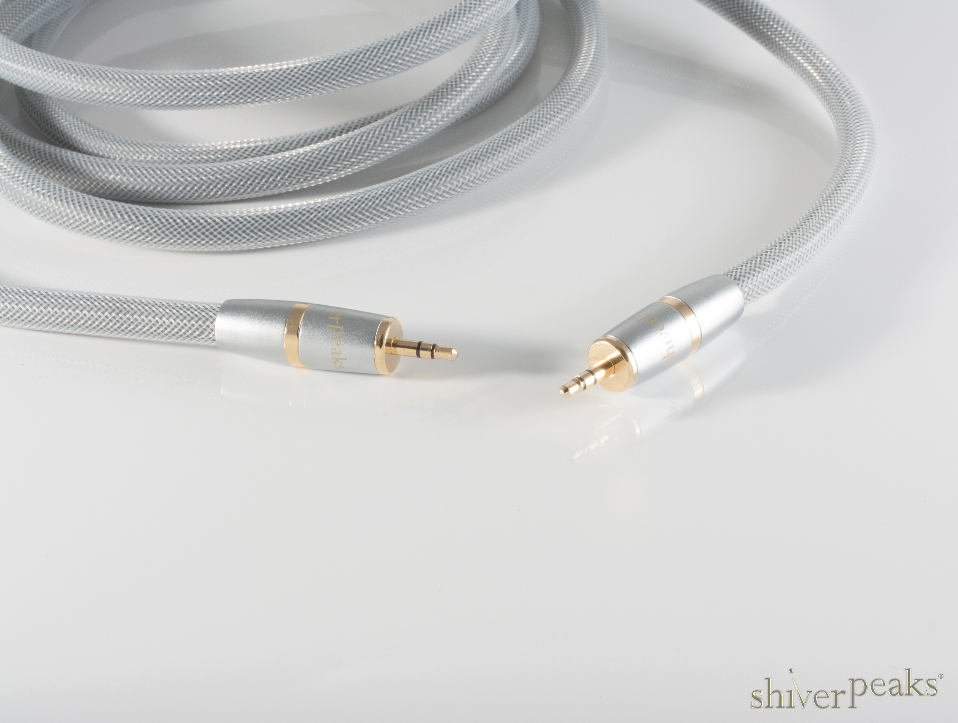 Ein silbernes Audiokabel mit vergoldeten 3,5-mm-Klinkensteckern liegt auf glänzender weißer Oberfläche.