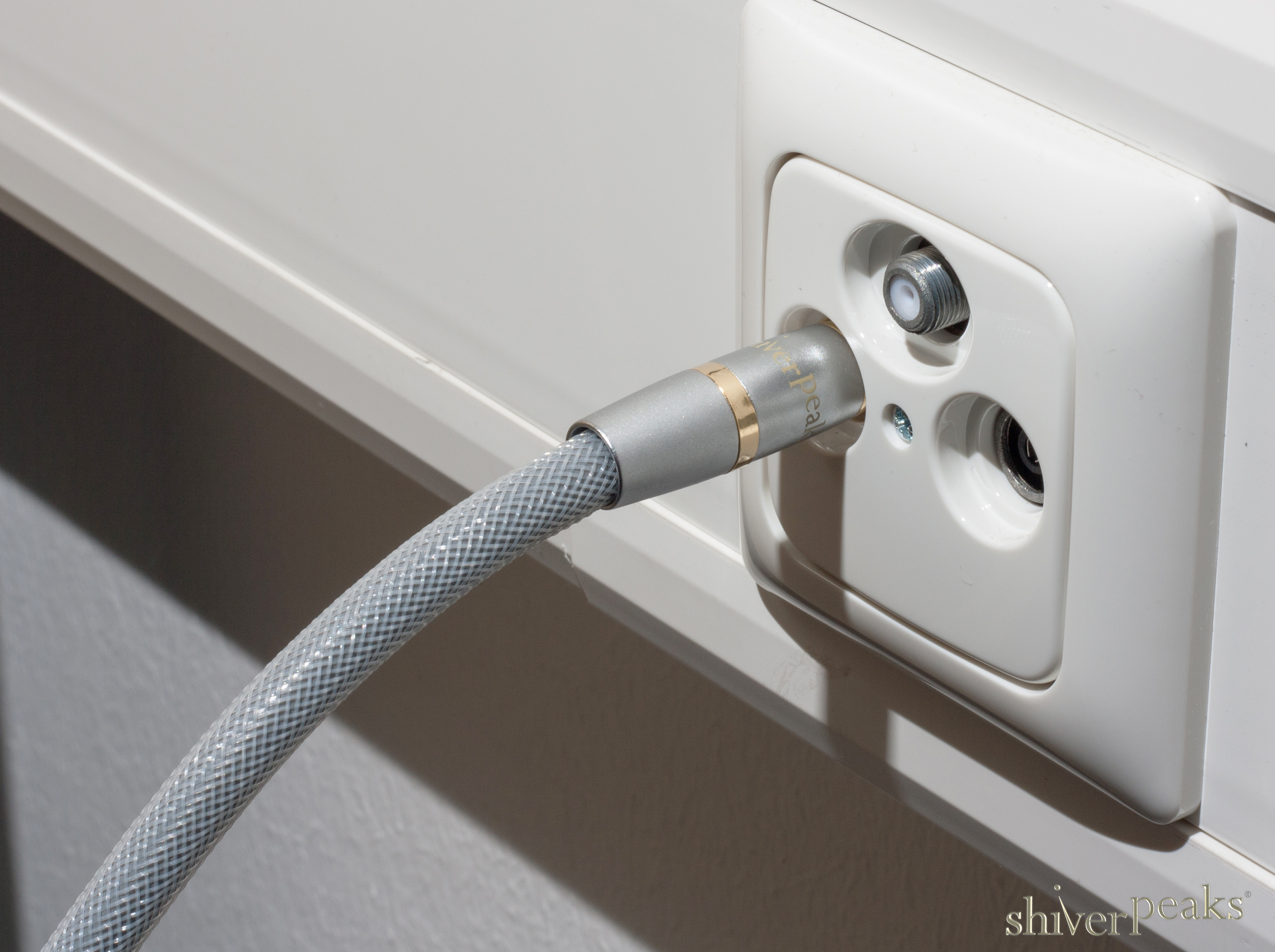 Ein graues Koaxialkabel ist in eine weiße Antennendose eingesteckt.