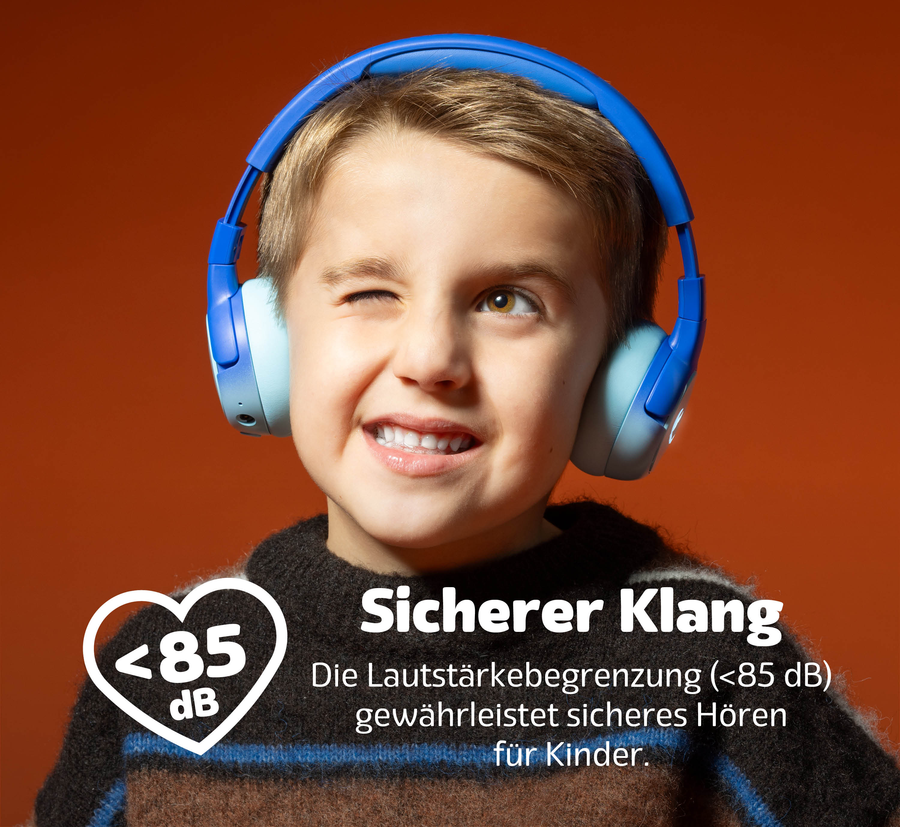 Ein Junge mit blauen Kopfhörern lächelt. Text unten: Sicherer Klang, <lt/>85 dB.