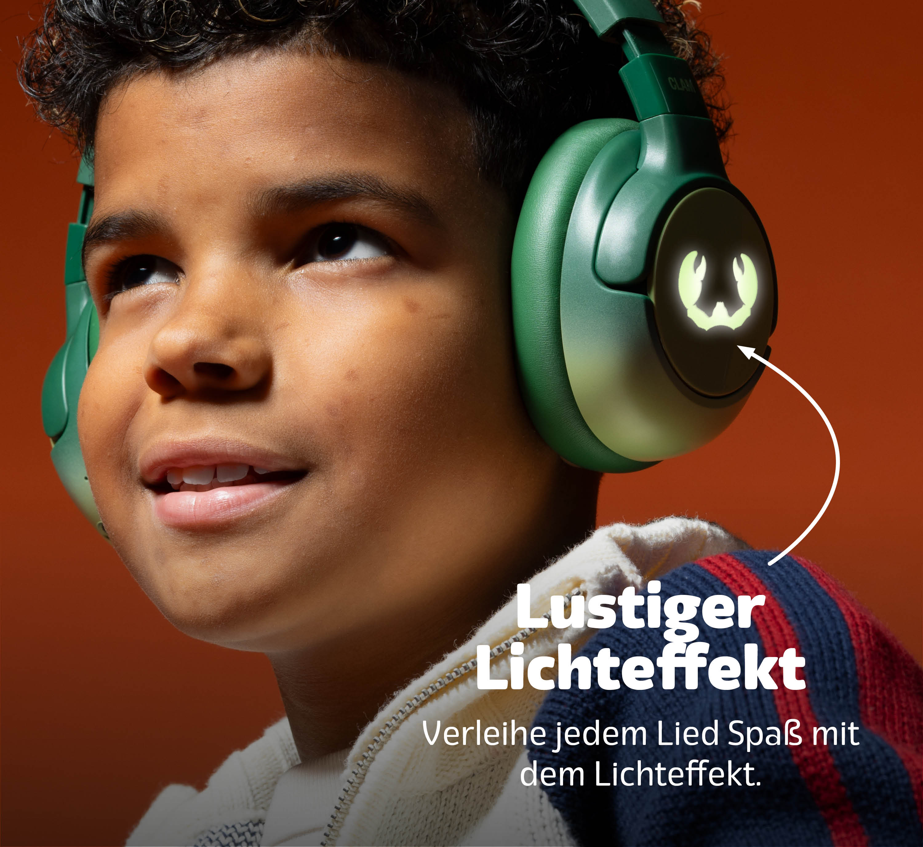 Ein Junge trägt grüne Kopfhörer mit leuchtenden Ohrmuscheln vor orangem Hintergrund.