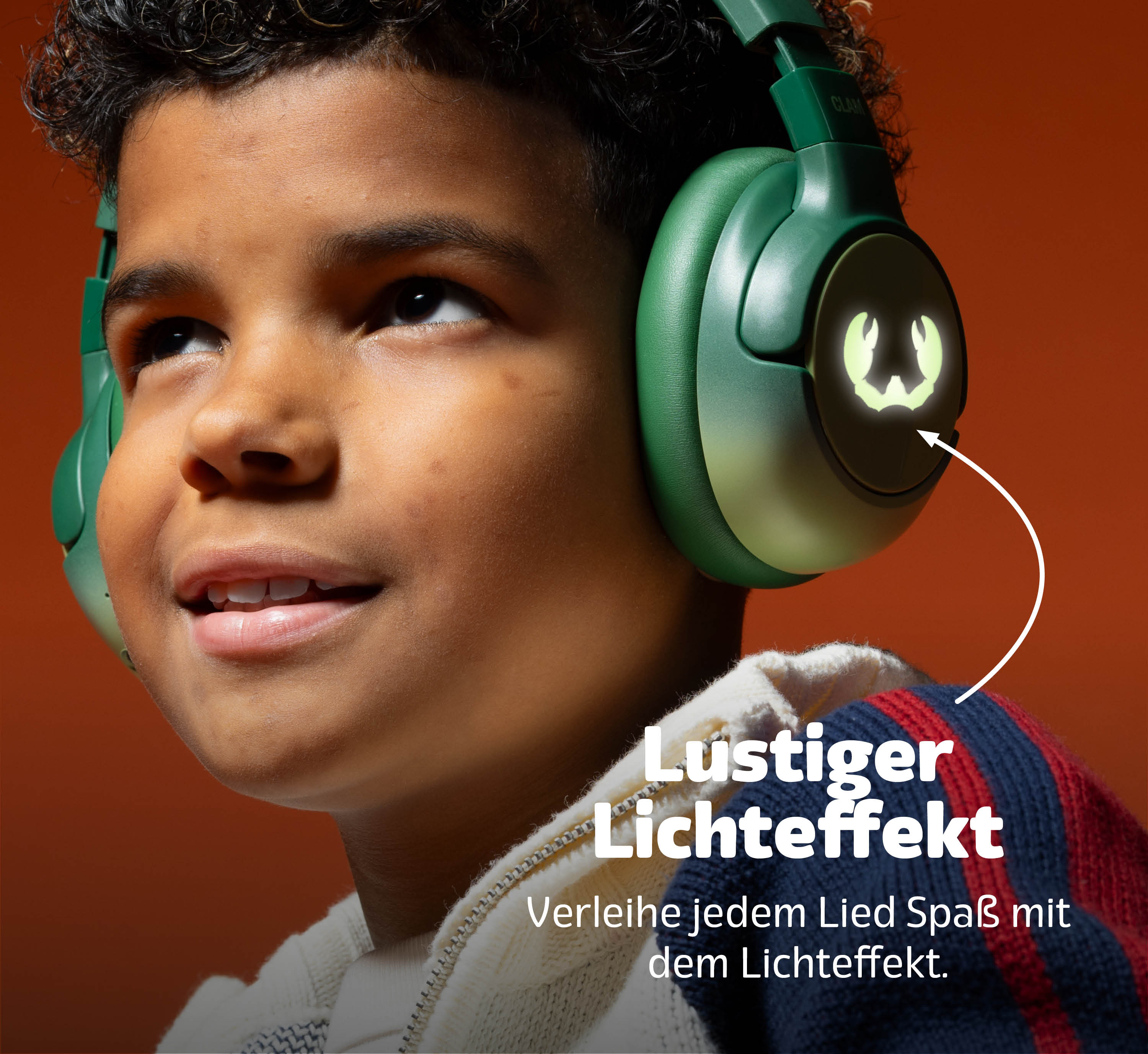 Ein Junge mit grünen Kopfhörern und leuchtendem Logo lächelt vor orangefarbenem Hintergrund.