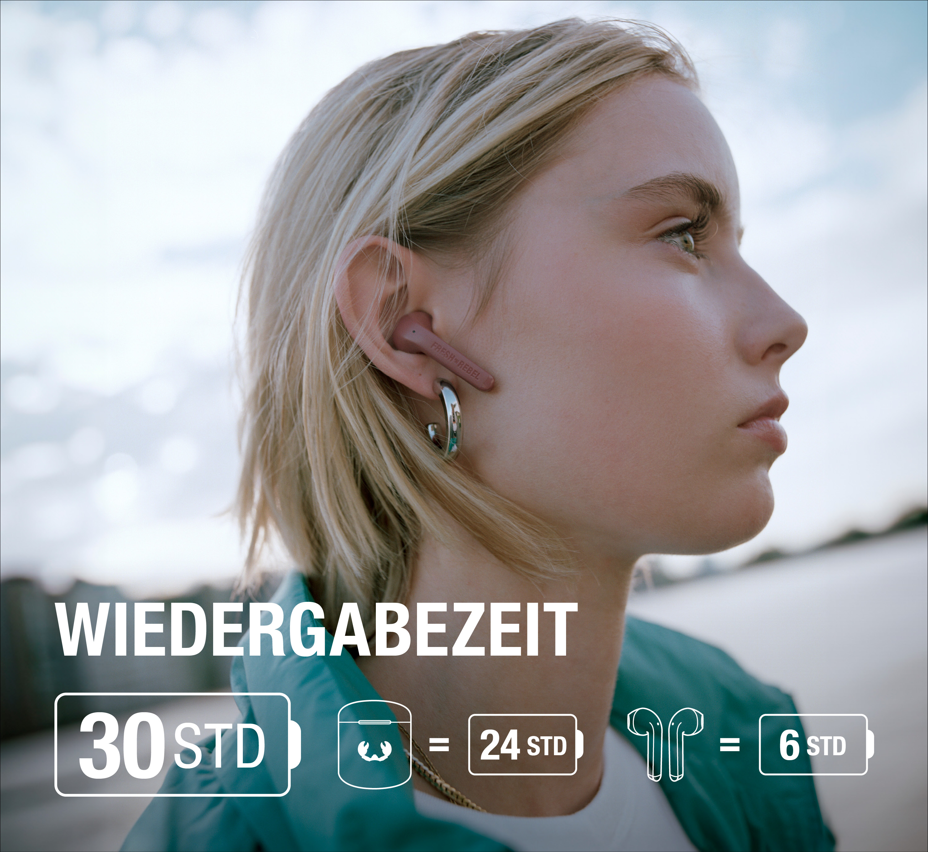 Blonde Frau trägt pinke Ohrhörer und Creolen vor bewölktem Himmel.