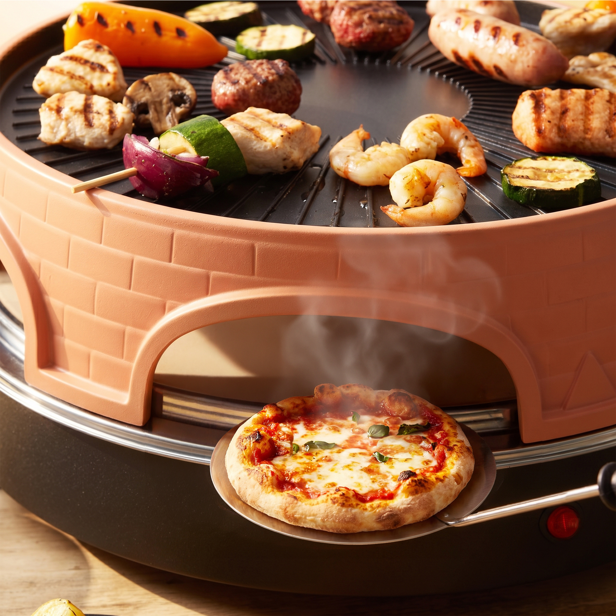 Una griglia da tavolo cuoce carne e verdure, mentre sotto si cuoce una pizza.