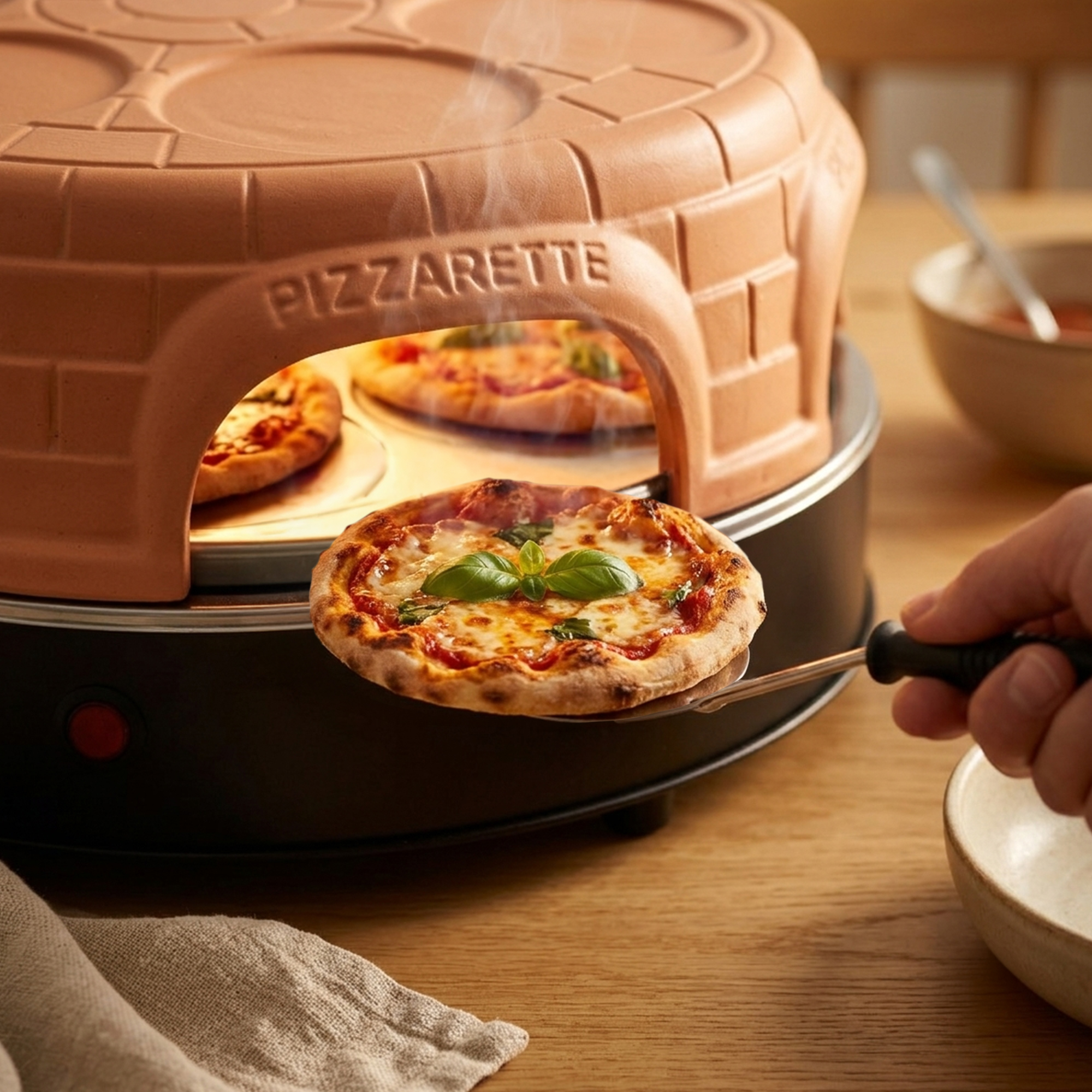 Una mano usa una espátula para colocar una pizza pequeña recién horneada con albahaca en un horno de terracota.
