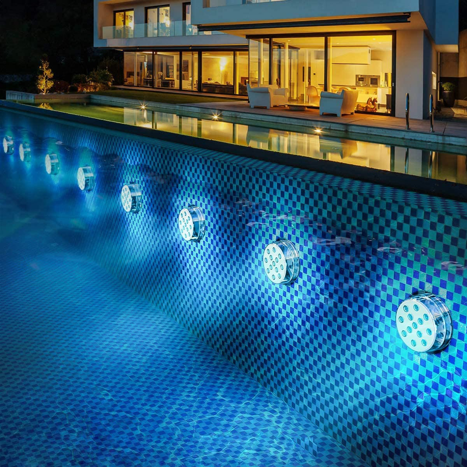 Ein gefliester Pool bei Nacht, beleuchtet von blauen Unterwasserlichtern, mit einem modernen beleuchteten Haus im Hintergrund.