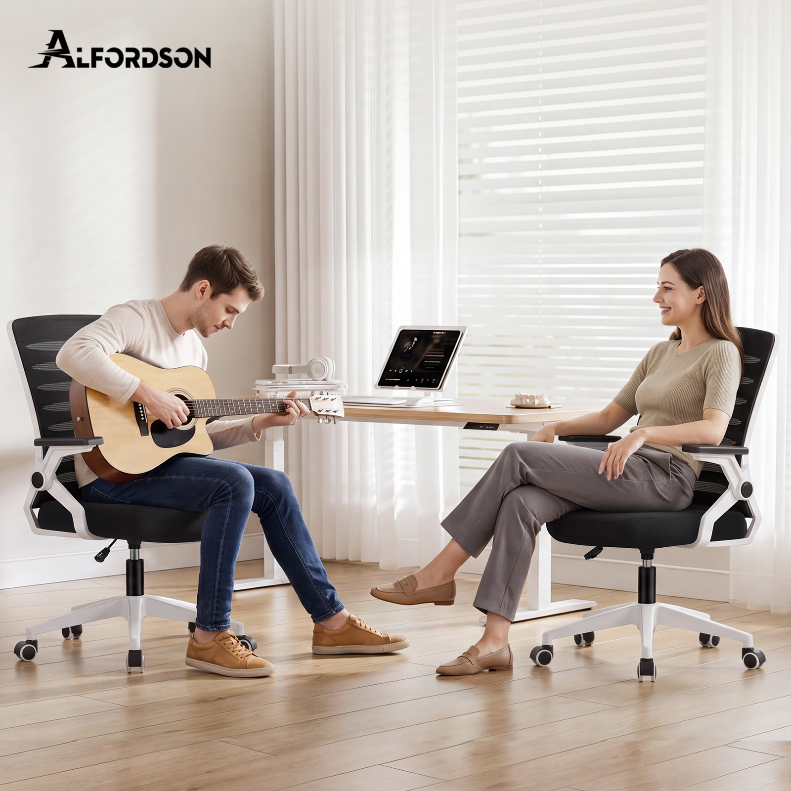 Un hombre toca la guitarra sentado en una silla de oficina y una mujer se sienta frente a él en otra silla.